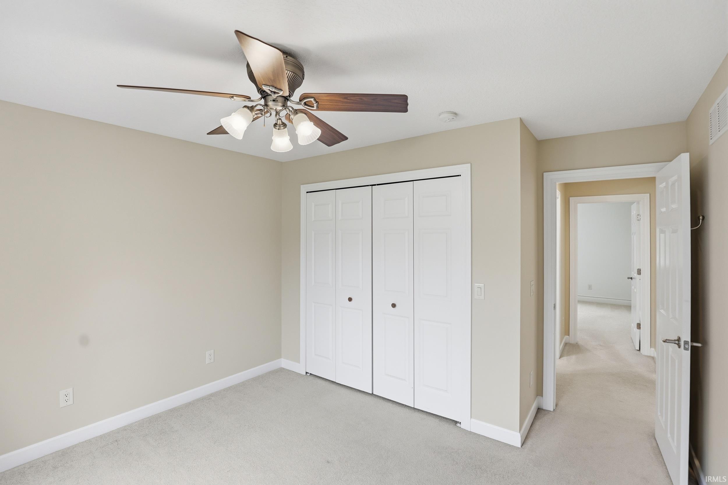 Unfurnished bedroom with light colored carpet, a closet, and a ceiling fan