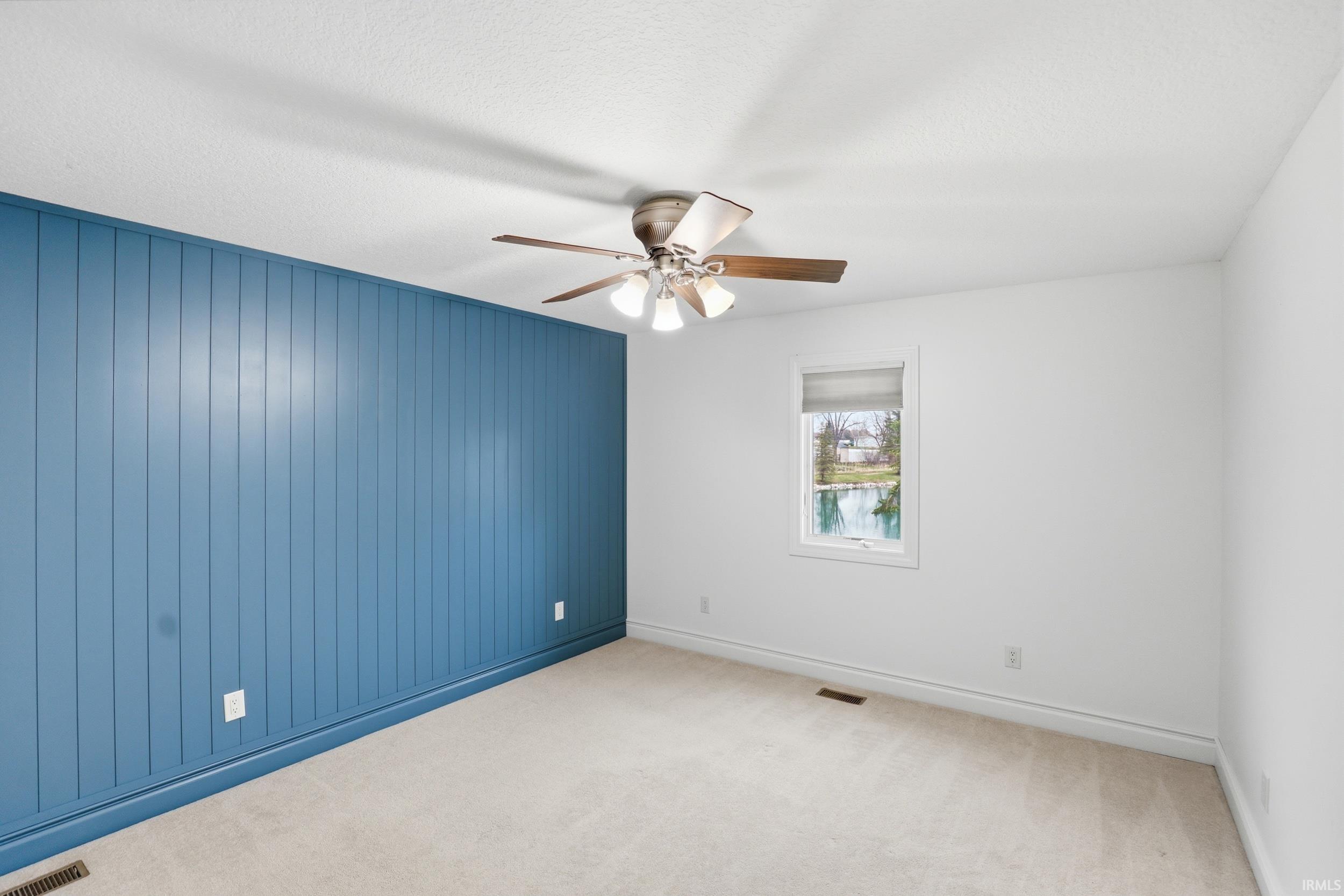 Unfurnished room featuring wooden walls, carpet, ceiling fan, and a textured ceiling