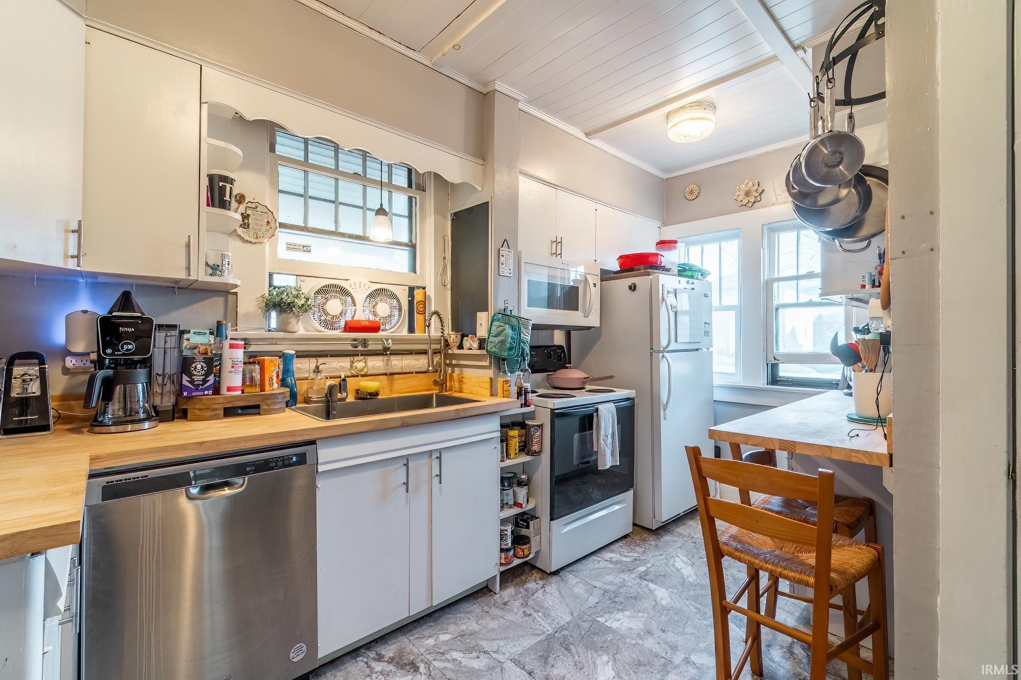 Kitchen with white appliances, white cabinetry, open shelves, crown molding, and butcher block counters