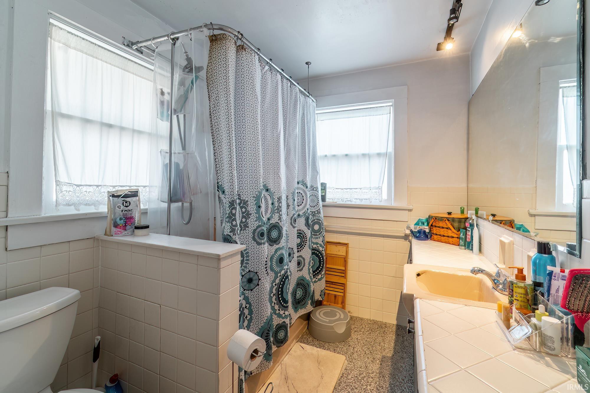 Bathroom featuring tile walls, vanity, a shower with curtain, speckle patterned floor, and plenty of natural light