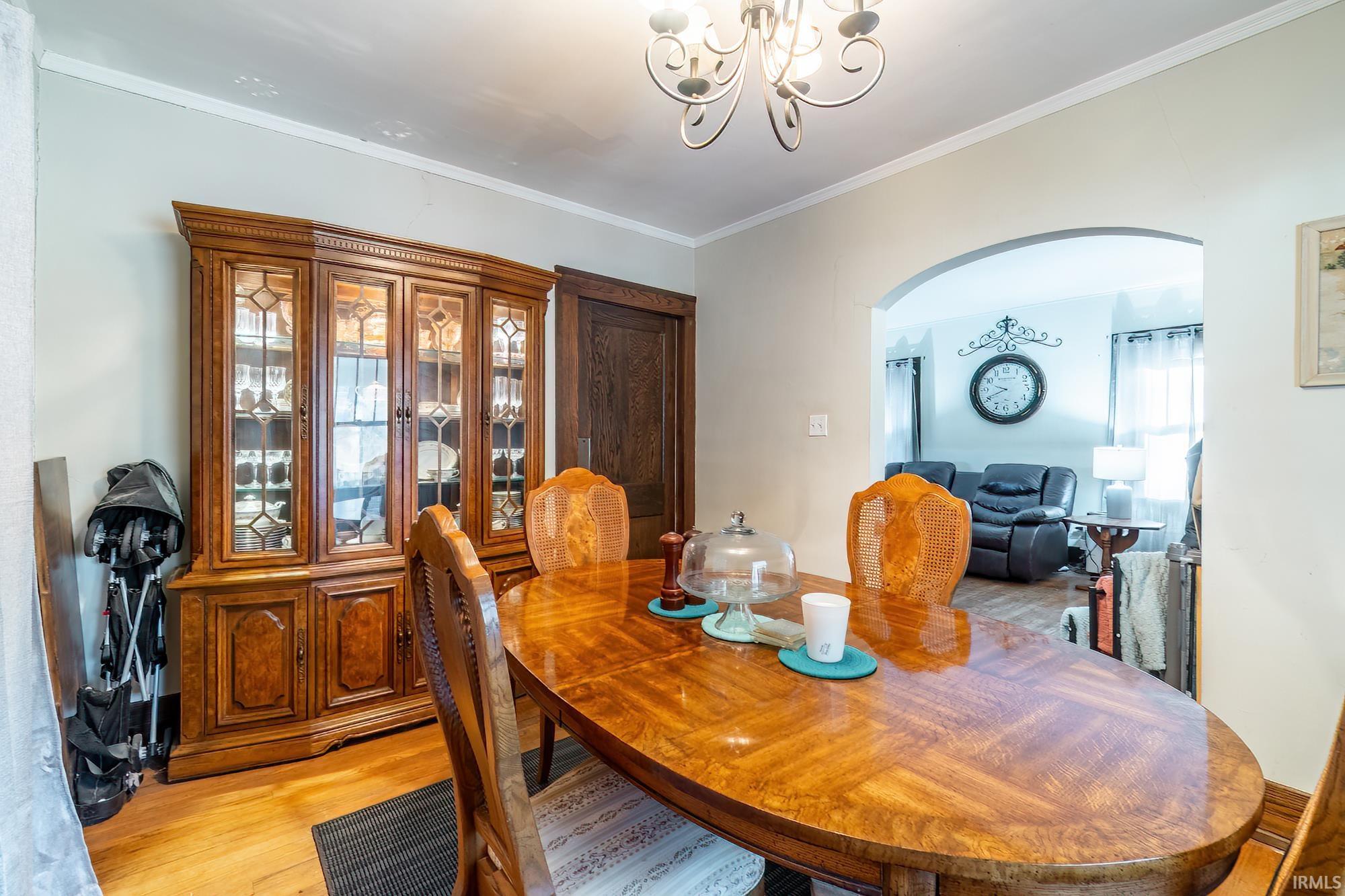 Dining room with light wood-style floors, arched walkways, a chandelier, and ornamental molding