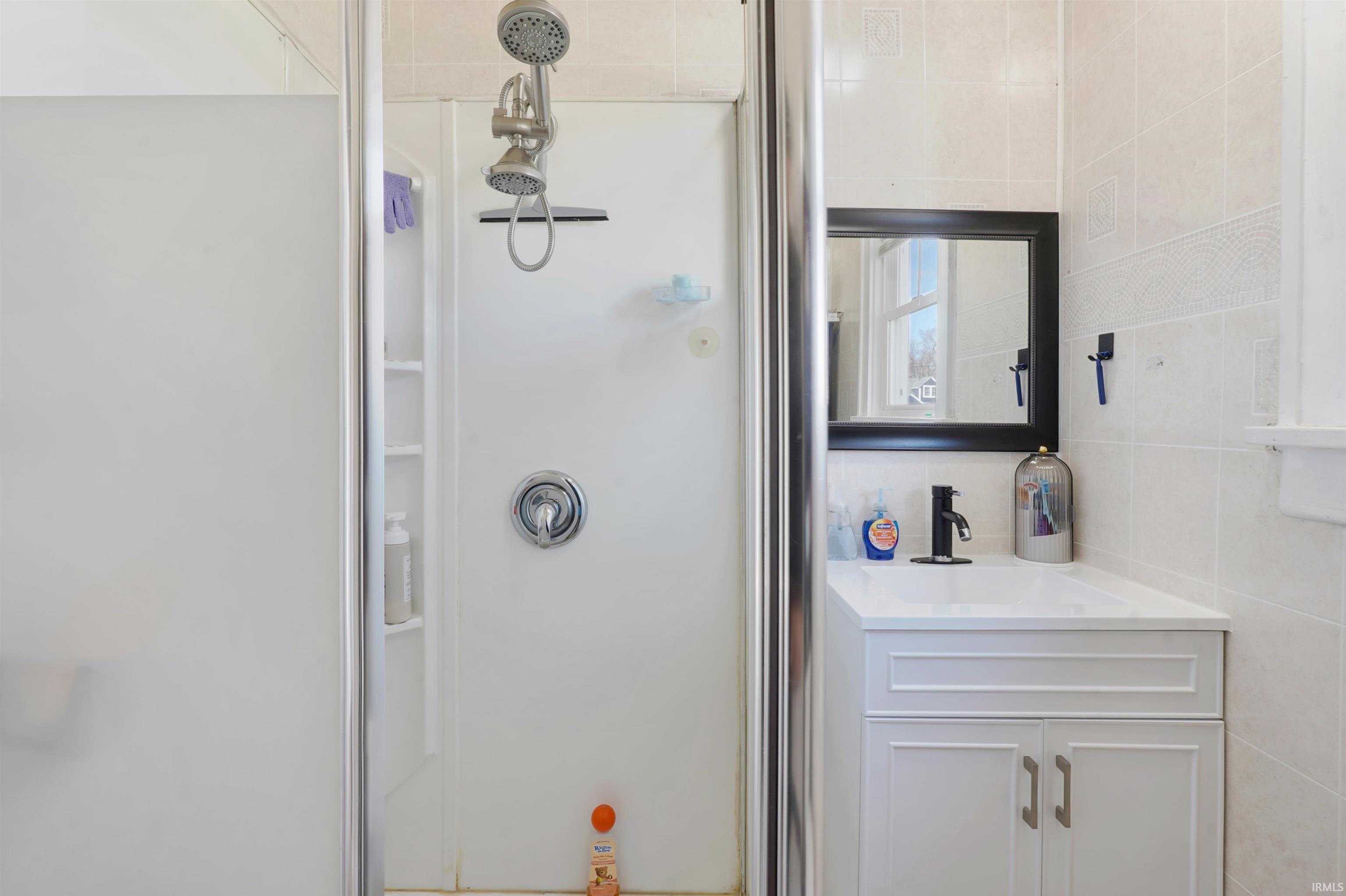 Bathroom with vanity, a stall shower, and tile walls