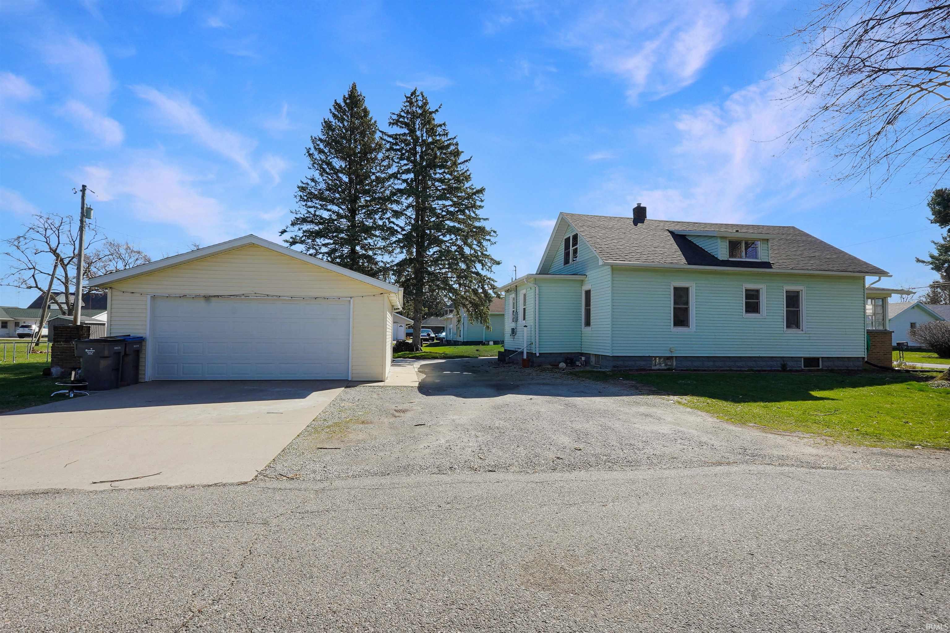 View of side of property featuring a shingled roof, an outdoor structure, a garage, a lawn, and a chimney