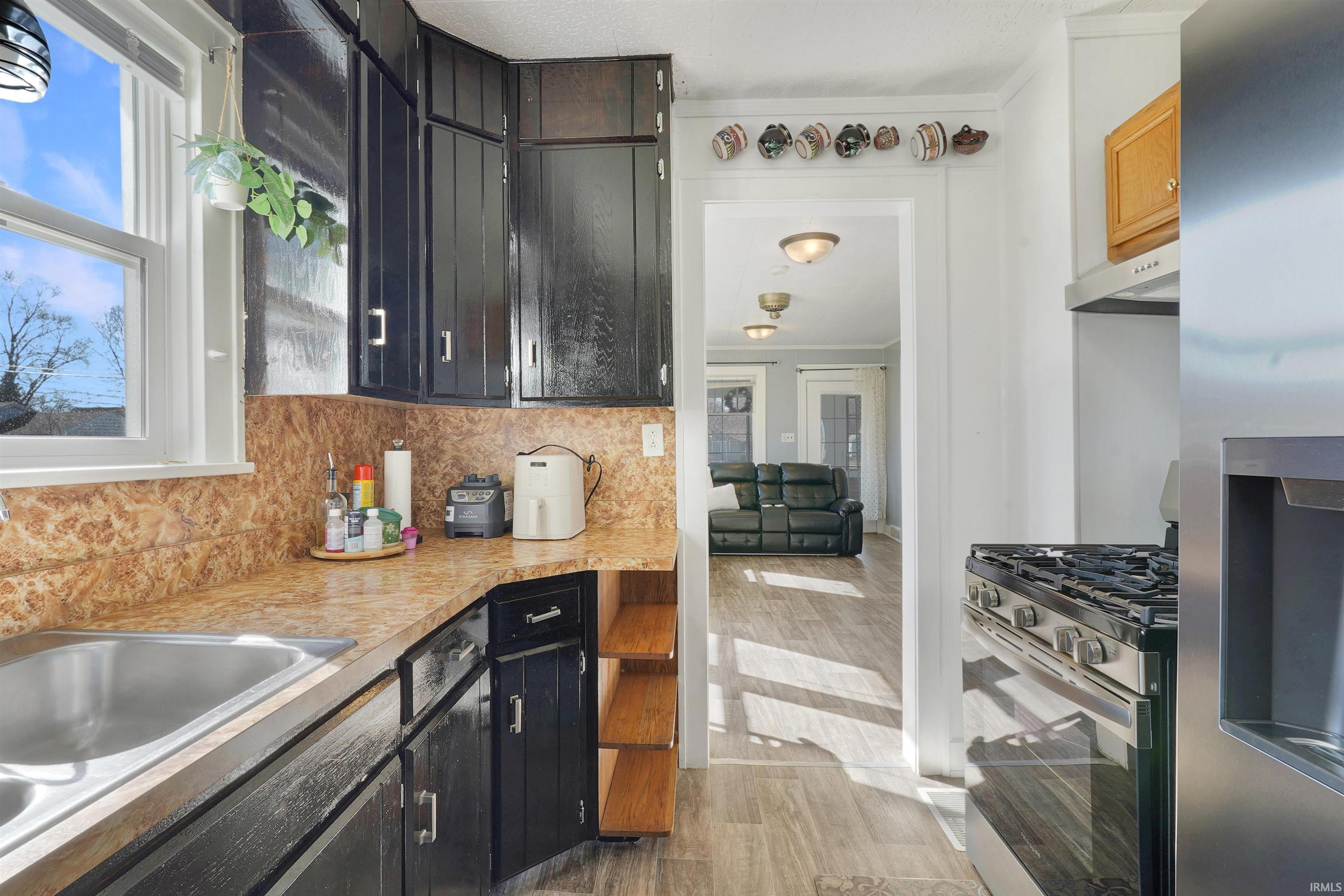 Kitchen featuring stainless steel appliances, dark cabinetry, backsplash, light wood-style floors, and light countertops