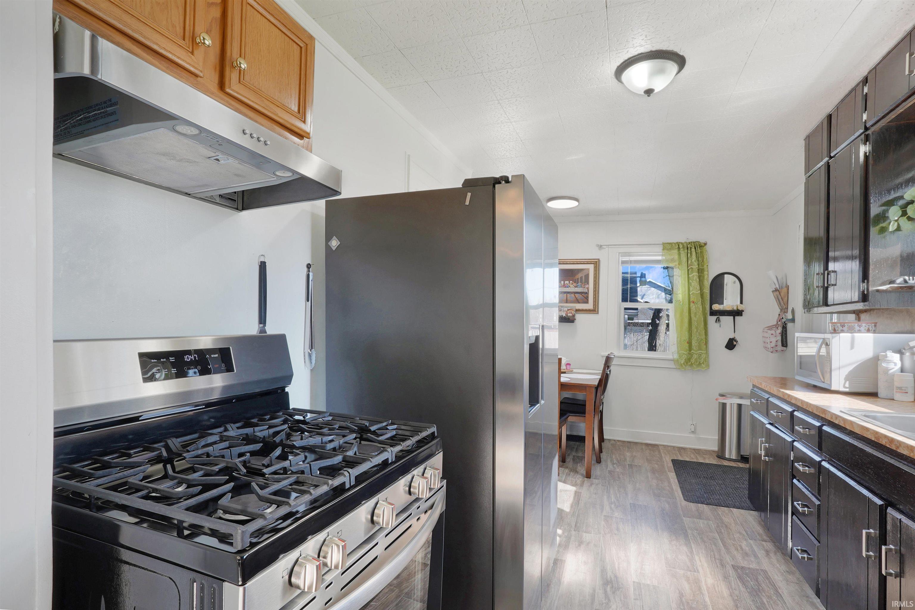 Kitchen with stainless steel appliances, light wood-type flooring, light countertops, and crown molding