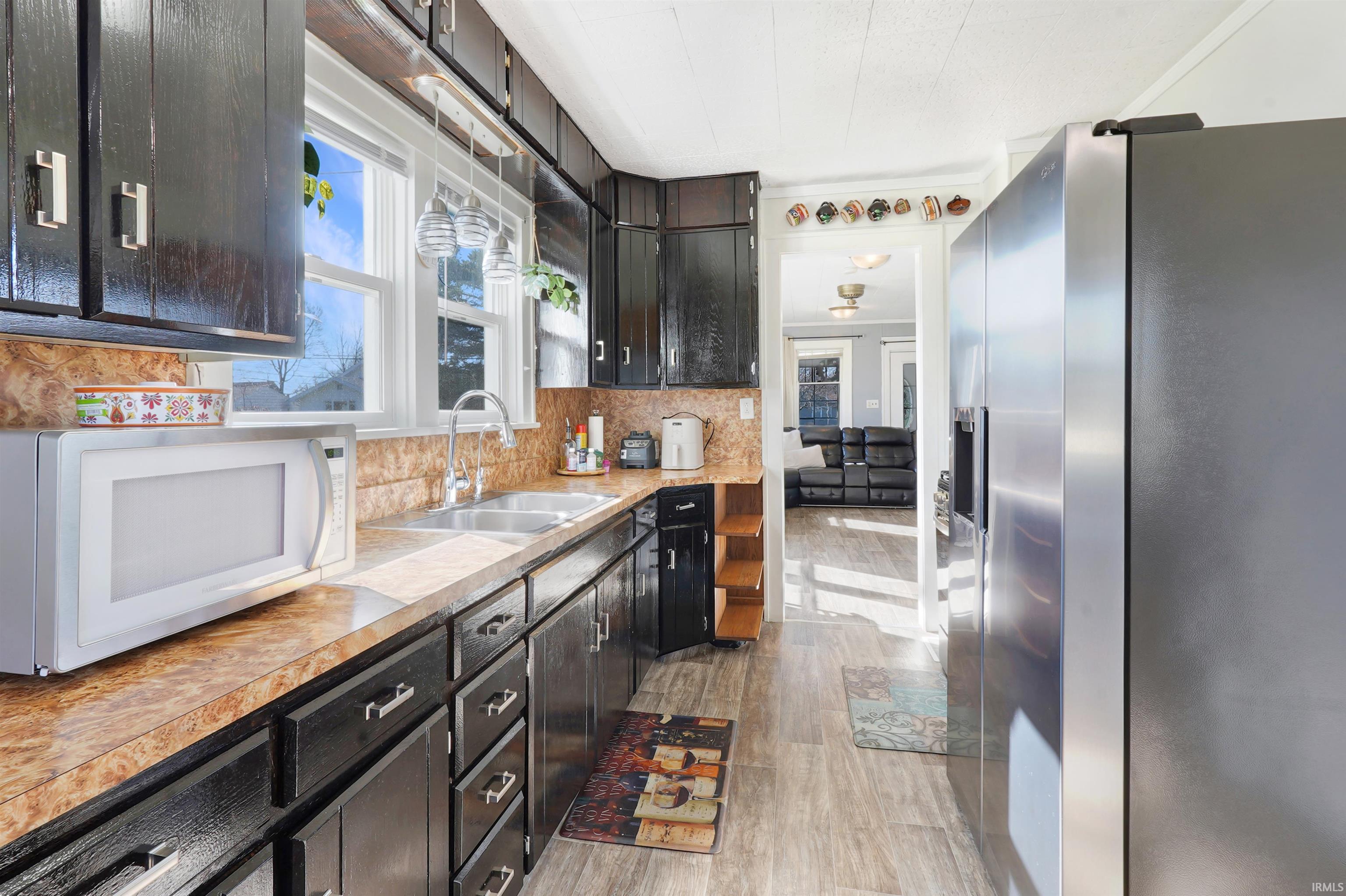 Kitchen featuring stainless steel fridge, dark cabinets, white microwave, tasteful backsplash, and light countertops