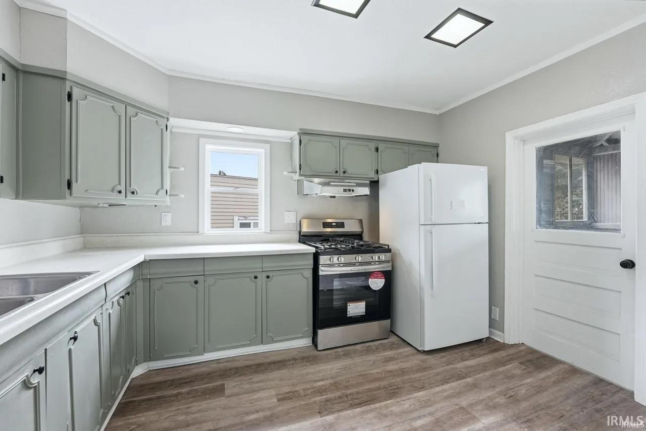 Kitchen with gas stove, light countertops, freestanding refrigerator, crown molding, and green cabinetry