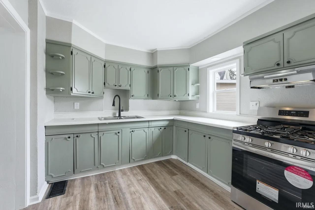 Kitchen featuring stainless steel gas range oven, light countertops, green cabinets, light wood-style flooring, and ornamental molding