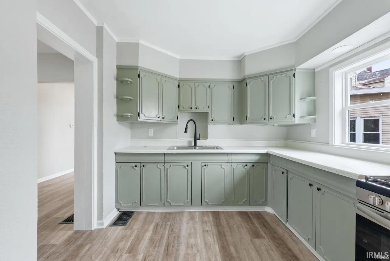 Kitchen featuring light countertops, green cabinetry, open shelves, light wood-style flooring, and ornamental molding