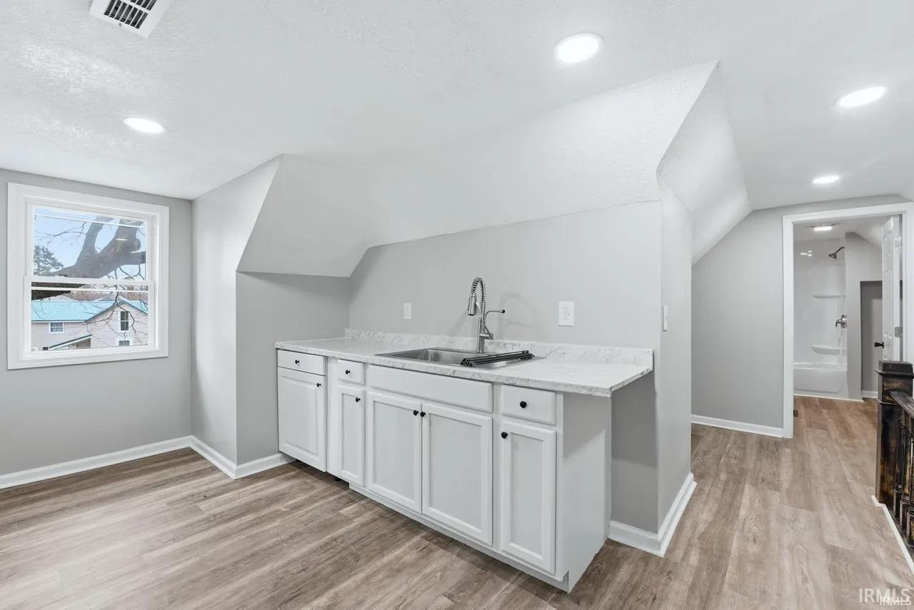 Bar with white cabinetry, light wood-type flooring, recessed lighting, and vaulted ceiling