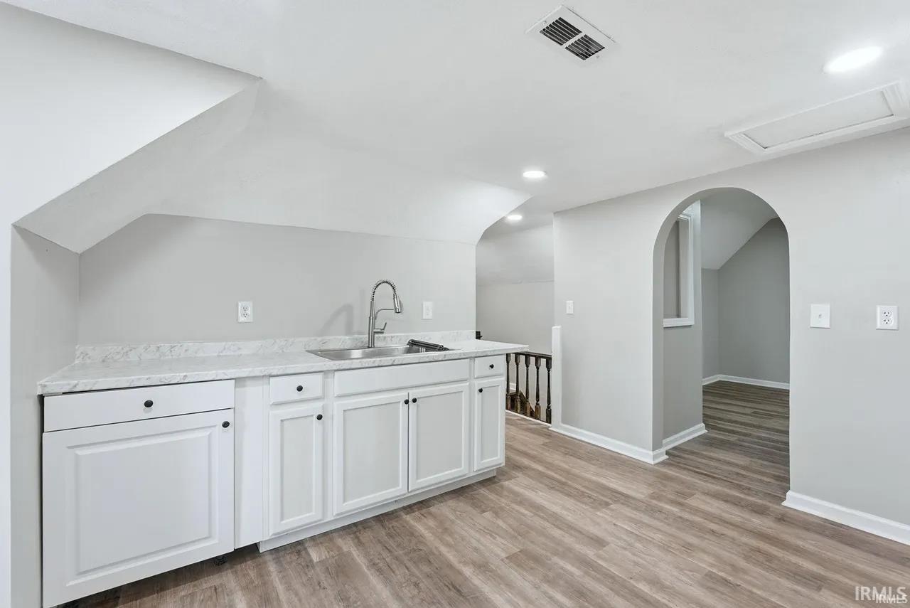 Bar with white cabinetry, vaulted ceiling, light wood finished floors, recessed lighting, and arched walkways
