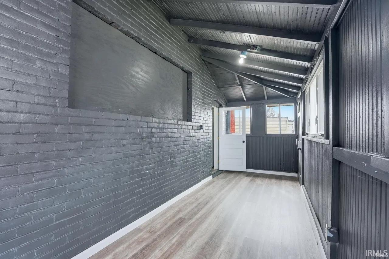 Entryway with brick wall, wood finished floors, and vaulted ceiling