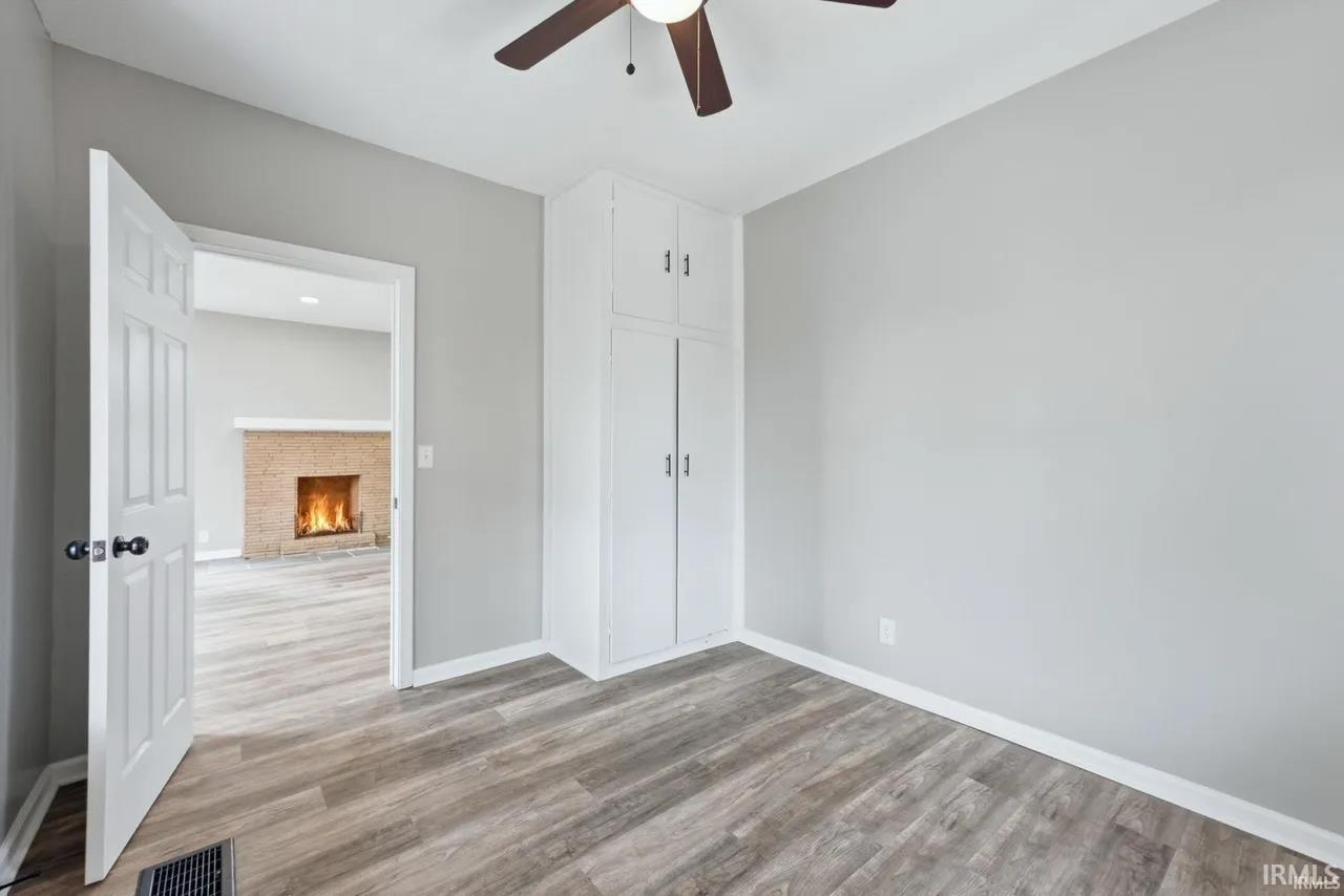 Unfurnished bedroom with a lit fireplace, light wood-style flooring, and ceiling fan