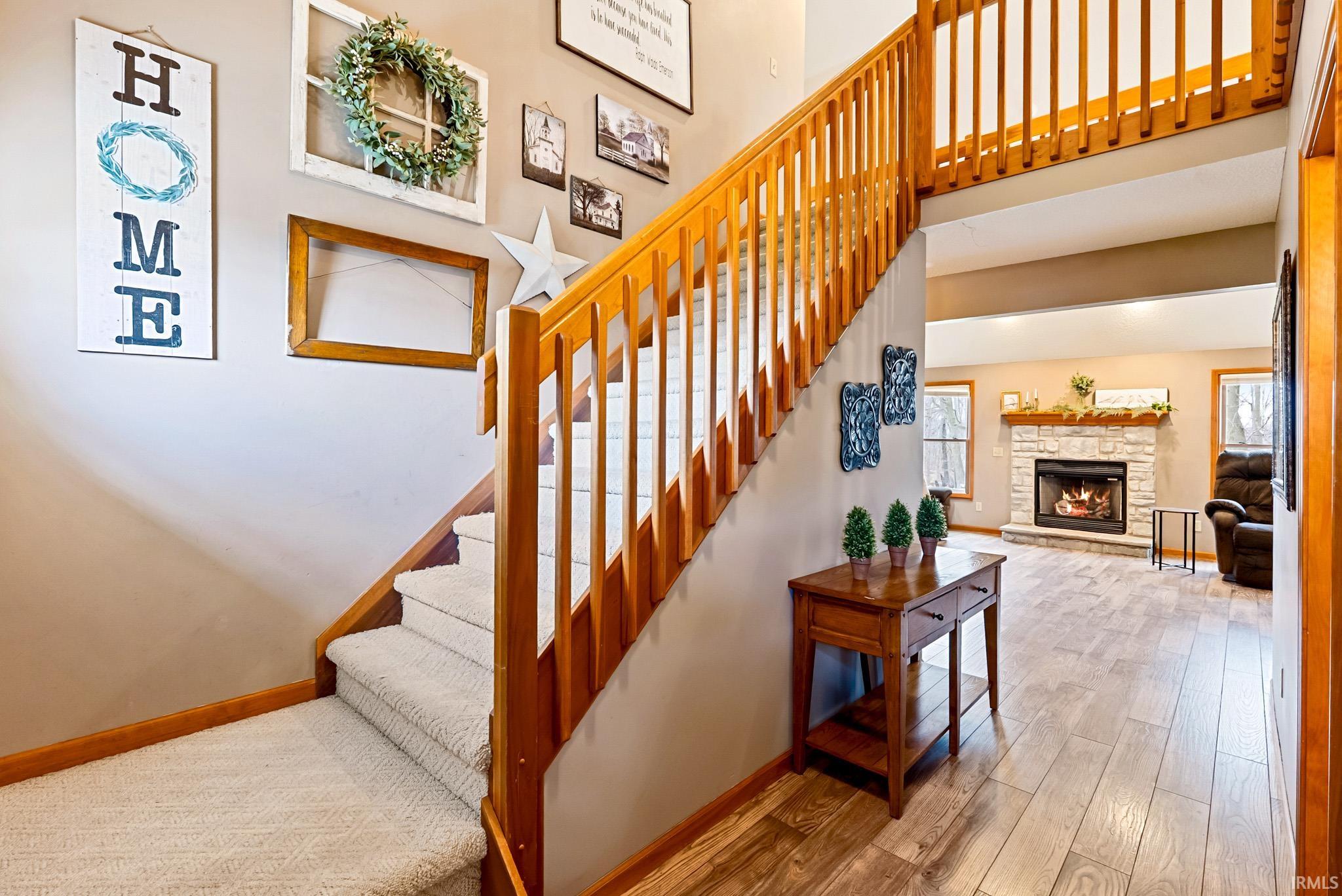 Staircase with wood-type flooring, a stone fireplace, and a high ceiling