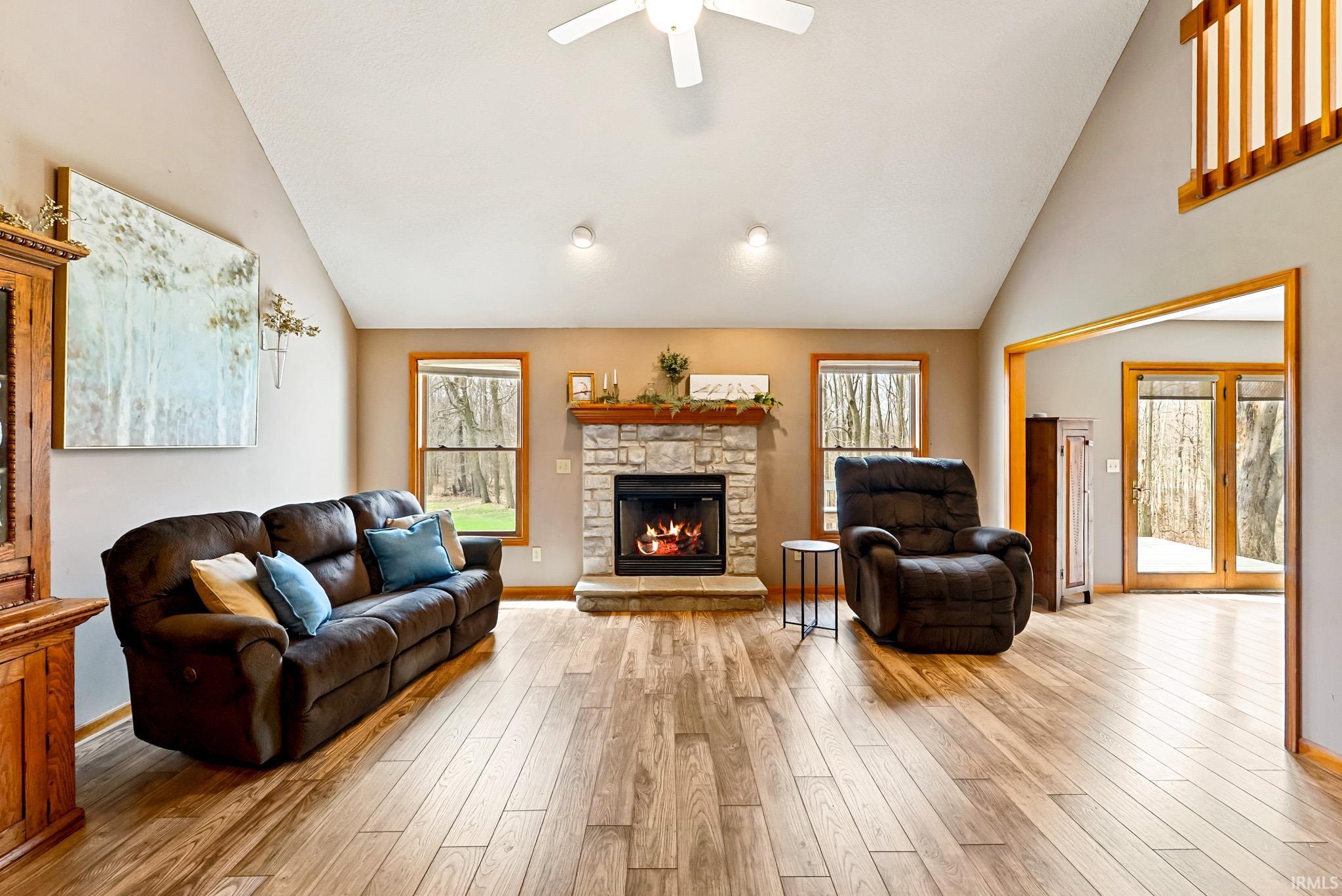 Living area with a fireplace, lofted ceiling, a ceiling fan, and light wood-style flooring