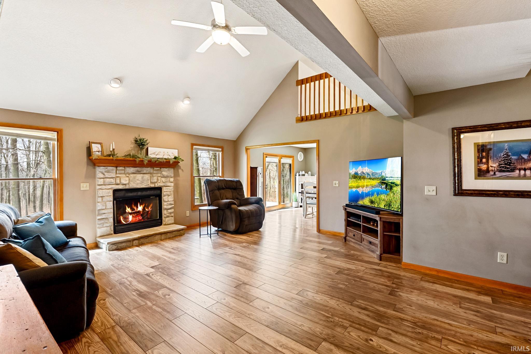 Living room featuring hardwood / wood-style floors, a stone fireplace, vaulted ceiling, and ceiling fan