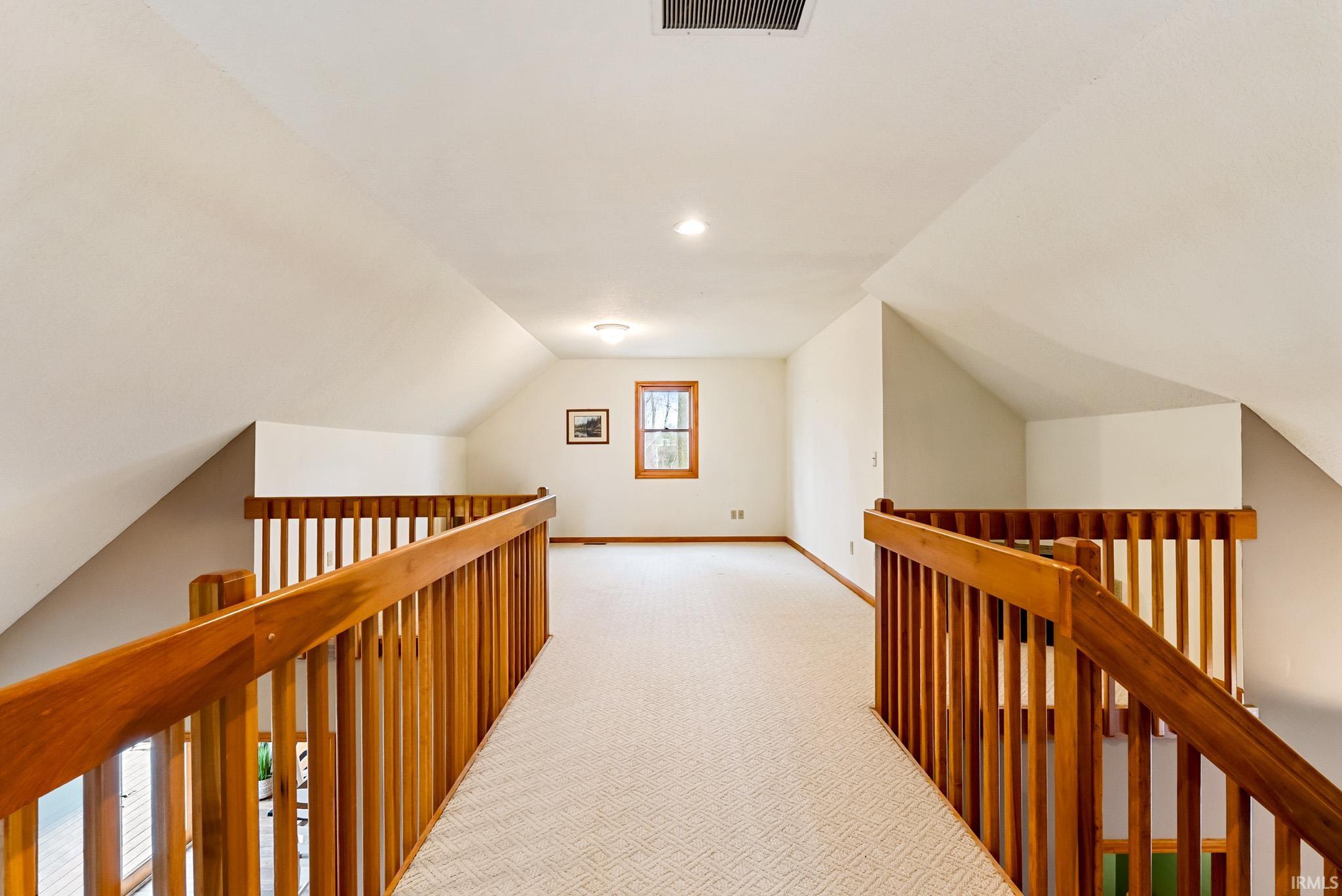 Hallway featuring lofted ceiling, light colored carpet, and an upstairs landing