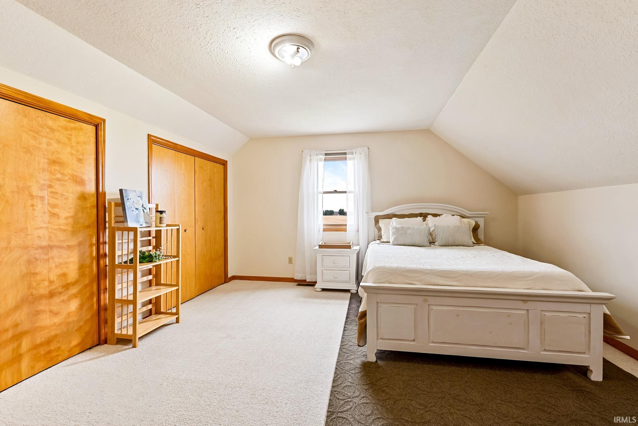 Bedroom featuring light colored carpet, a textured ceiling, and multiple closets