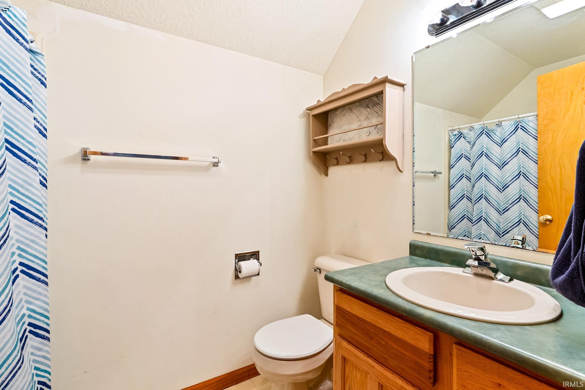 Full bathroom with curtained shower, vanity, and vaulted ceiling