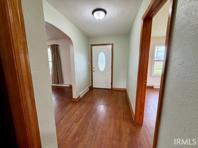 Entrance foyer with a textured wall, a textured ceiling, arched walkways, and dark wood-type flooring