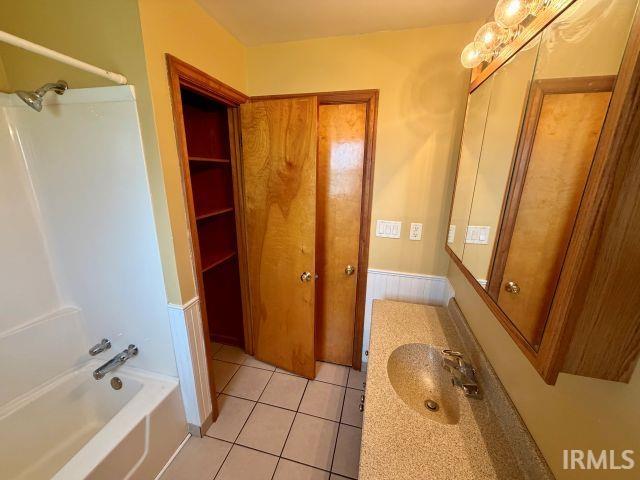 Bathroom with vanity,  shower combination, light tile patterned floors, and a wainscoted wall