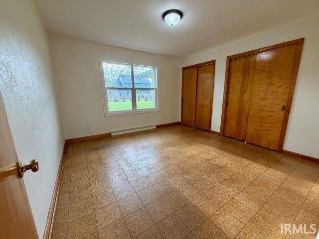Unfurnished bedroom featuring two closets, light floors, and a baseboard heating unit