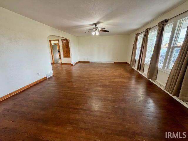 Empty room with arched walkways, dark wood-type flooring, and ceiling fan