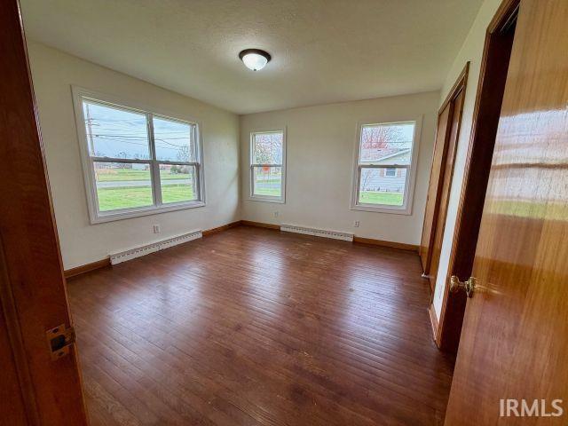 Spare room featuring dark wood-type flooring, a baseboard heating unit, and plenty of natural light