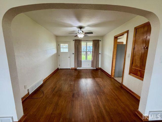 Doorway to outside featuring arched walkways, wood-type flooring, a textured wall, and ceiling fan