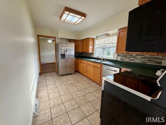 Kitchen featuring stainless steel fridge, black microwave, wood finish cabinetry, dark countertops, and light tile patterned floors