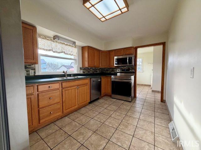 Kitchen featuring wood finish cabinets, healthy amount of natural light, dark countertops, and stainless steel appliances