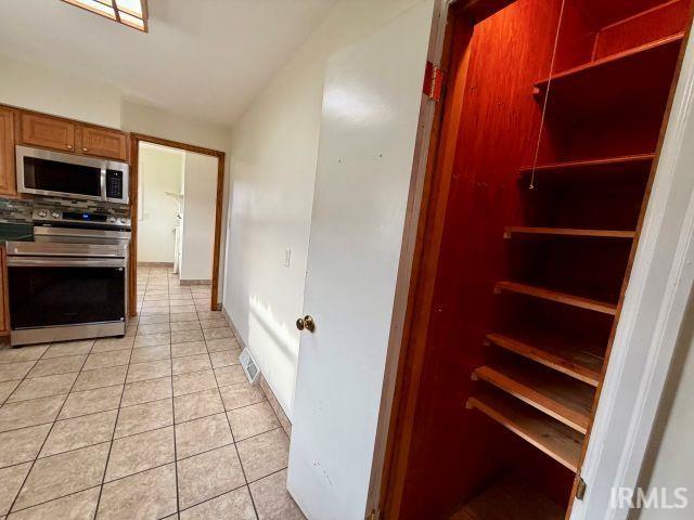 Kitchen with stainless steel appliances, light tile patterned floors, wood finish cabinets, and vaulted ceiling