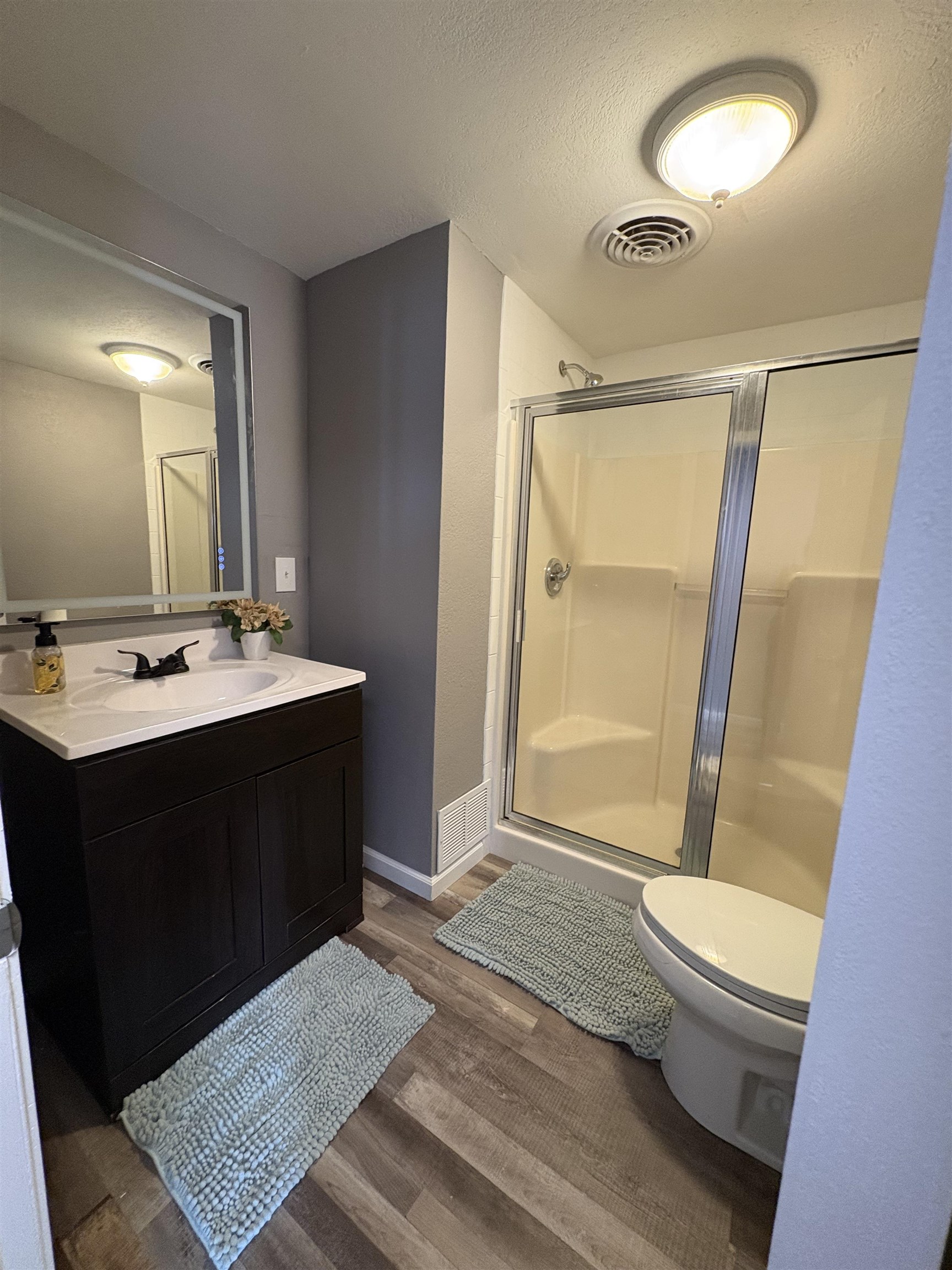 Full bathroom featuring vanity, a stall shower, dark wood finished floors, and a textured ceiling