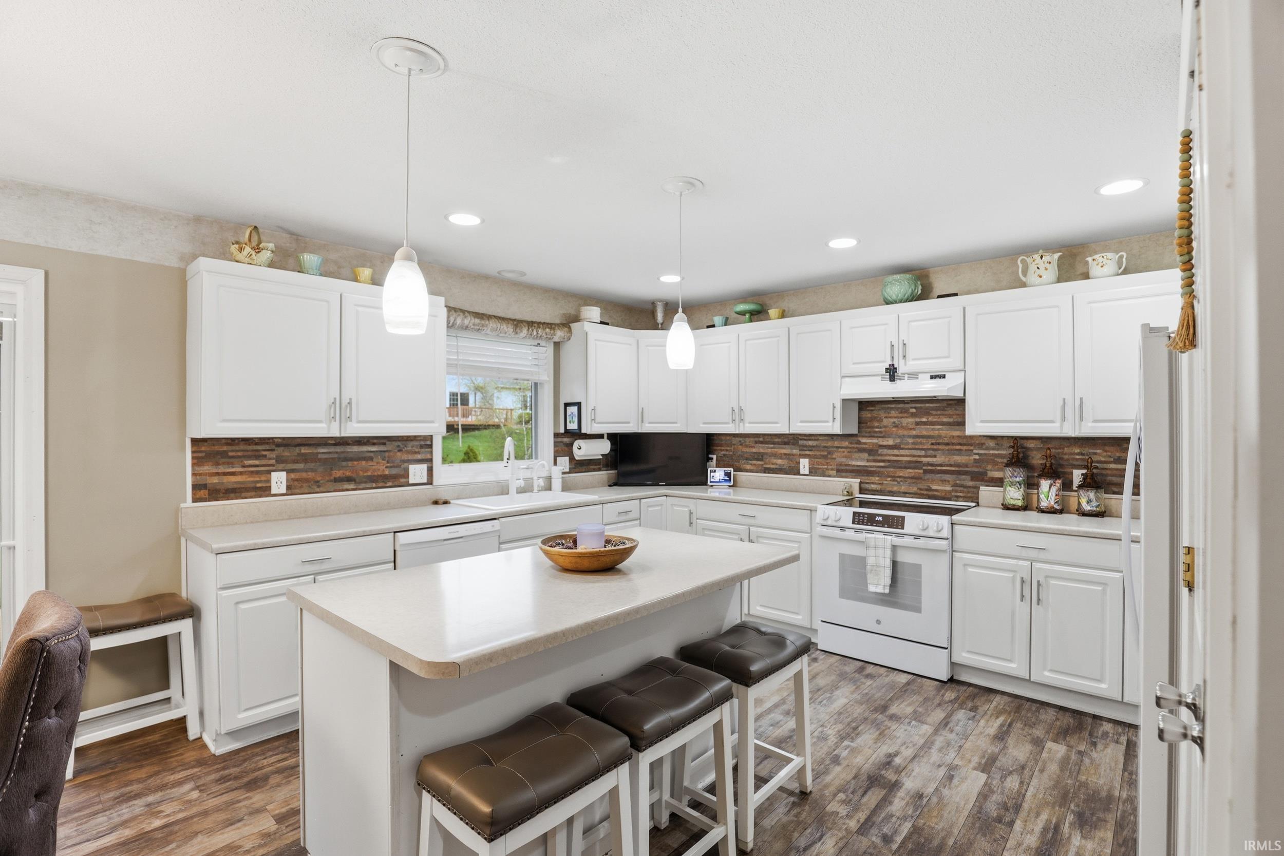 Kitchen with white cabinetry, white appliances, a breakfast bar area, light countertops, and dark wood finished floors