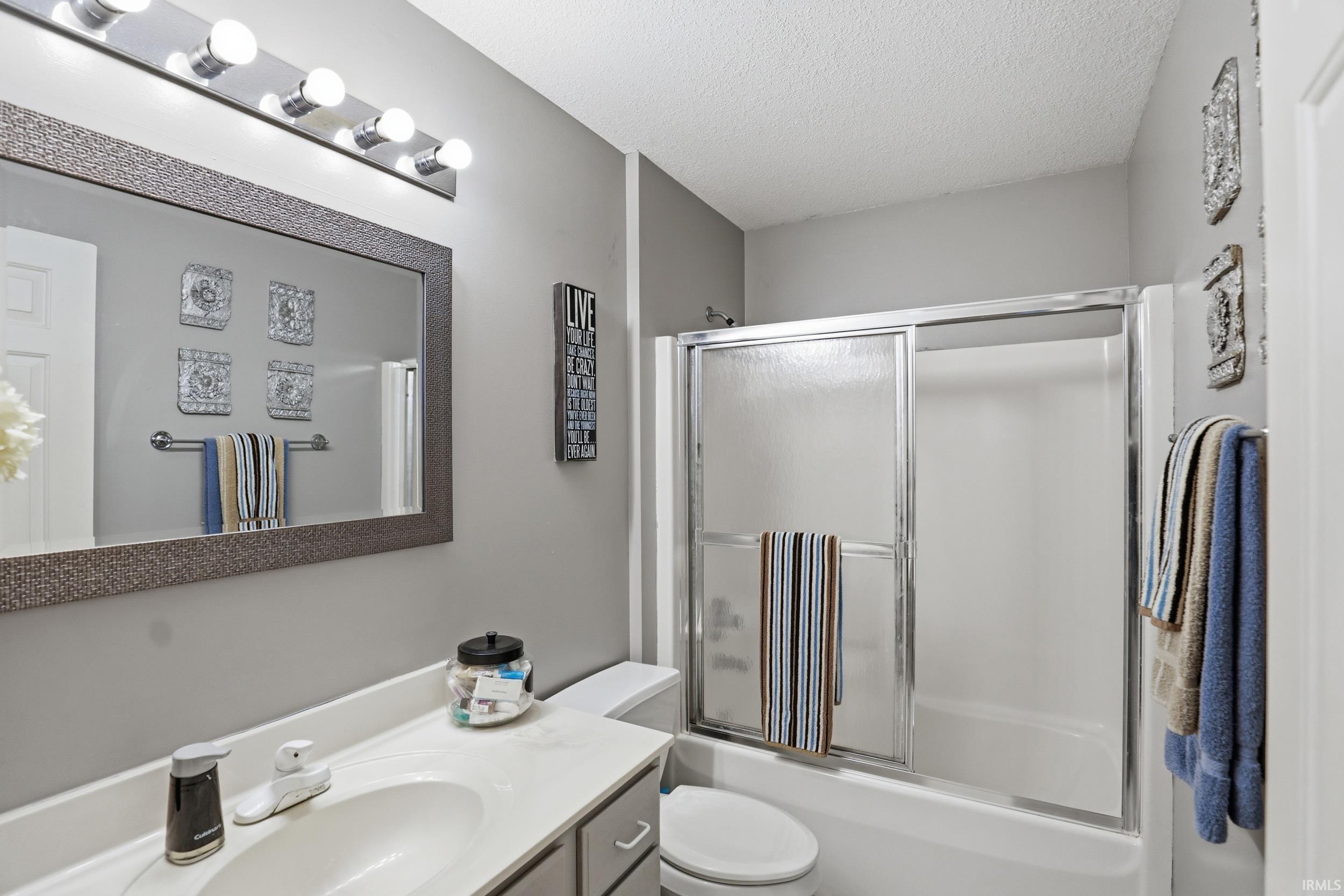 Bathroom with vanity, a textured ceiling, and combined bath / shower with glass door