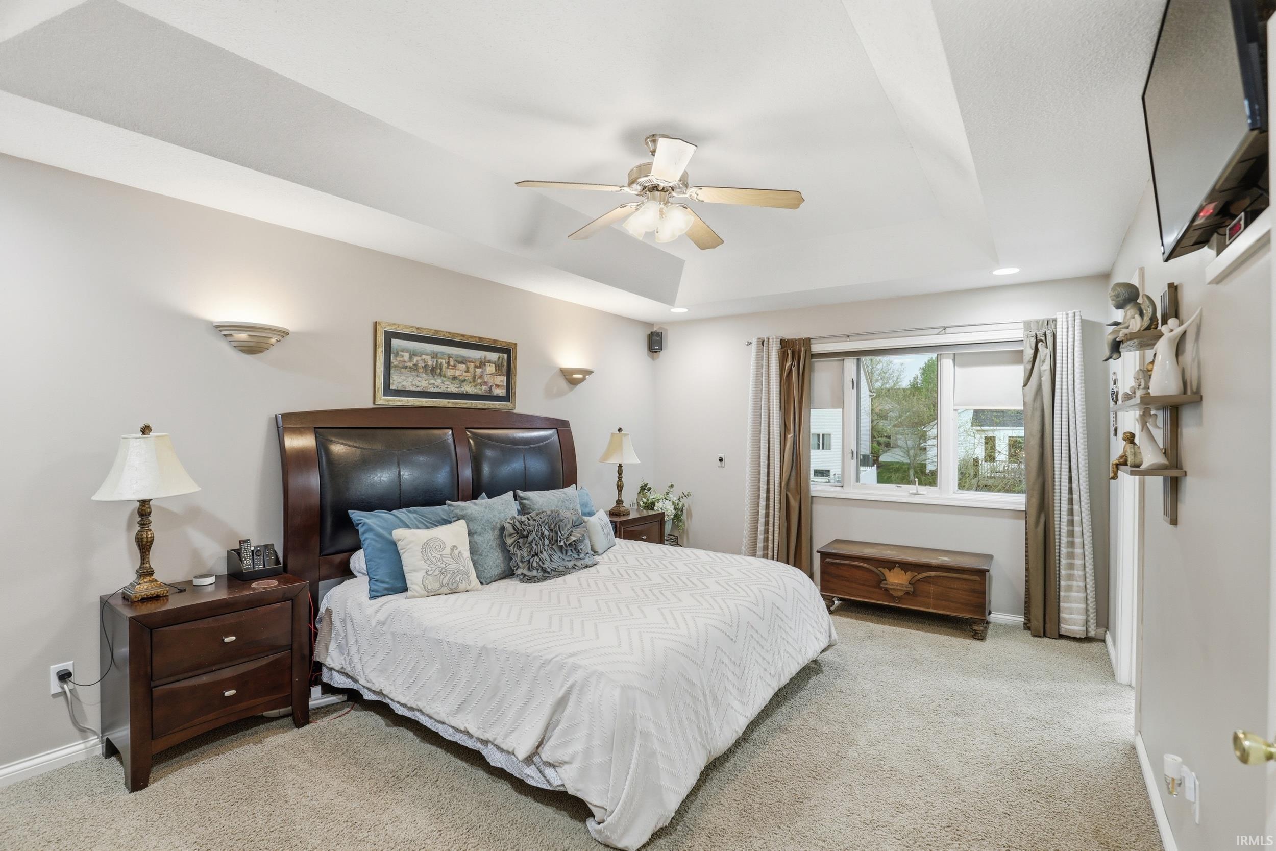 Bedroom with light carpet, a tray ceiling, and ceiling fan
