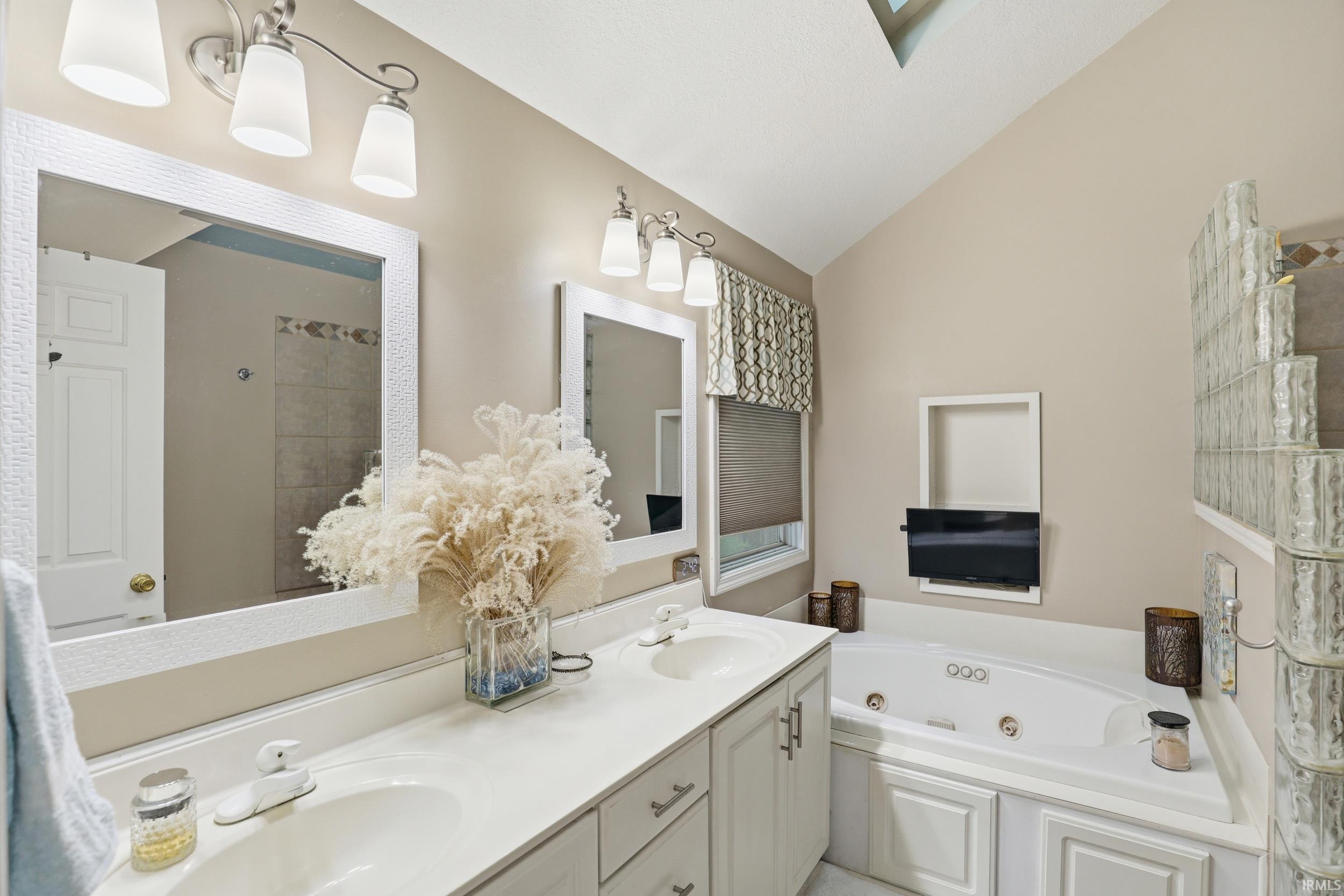 Full bathroom with vaulted ceiling, a tub with jets, and double vanity