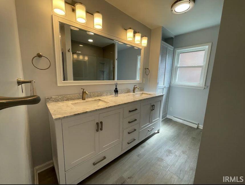 Bathroom with double vanity, updated shower, light wood-style flooring.