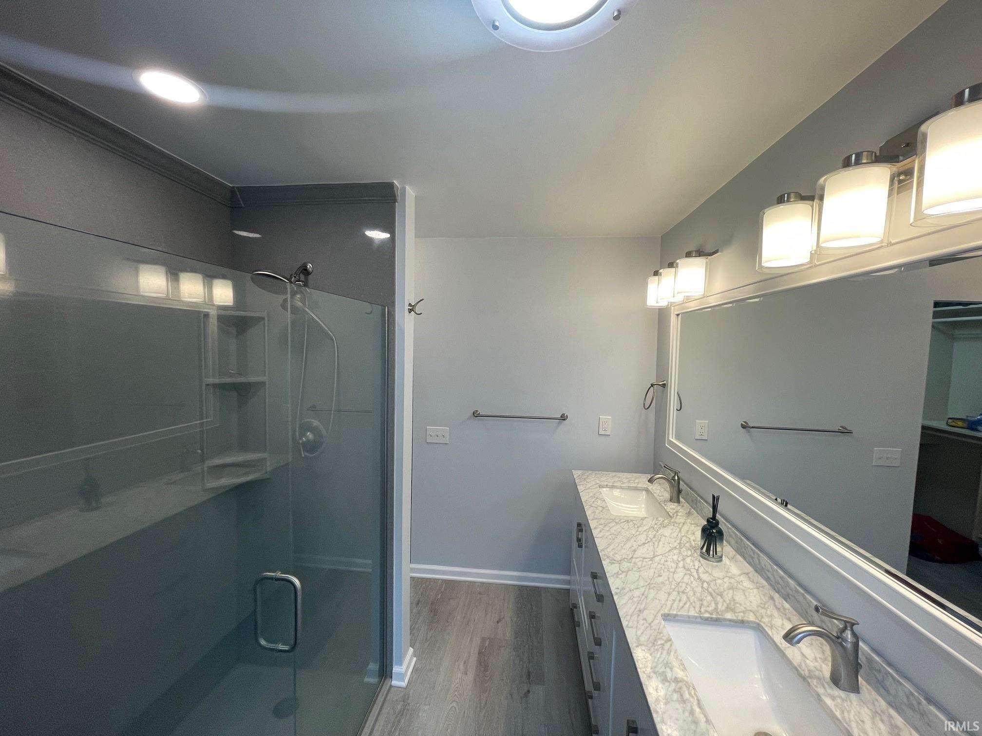 Bathroom featuring double vanity, dark wood finished floors, and a walk-in shower