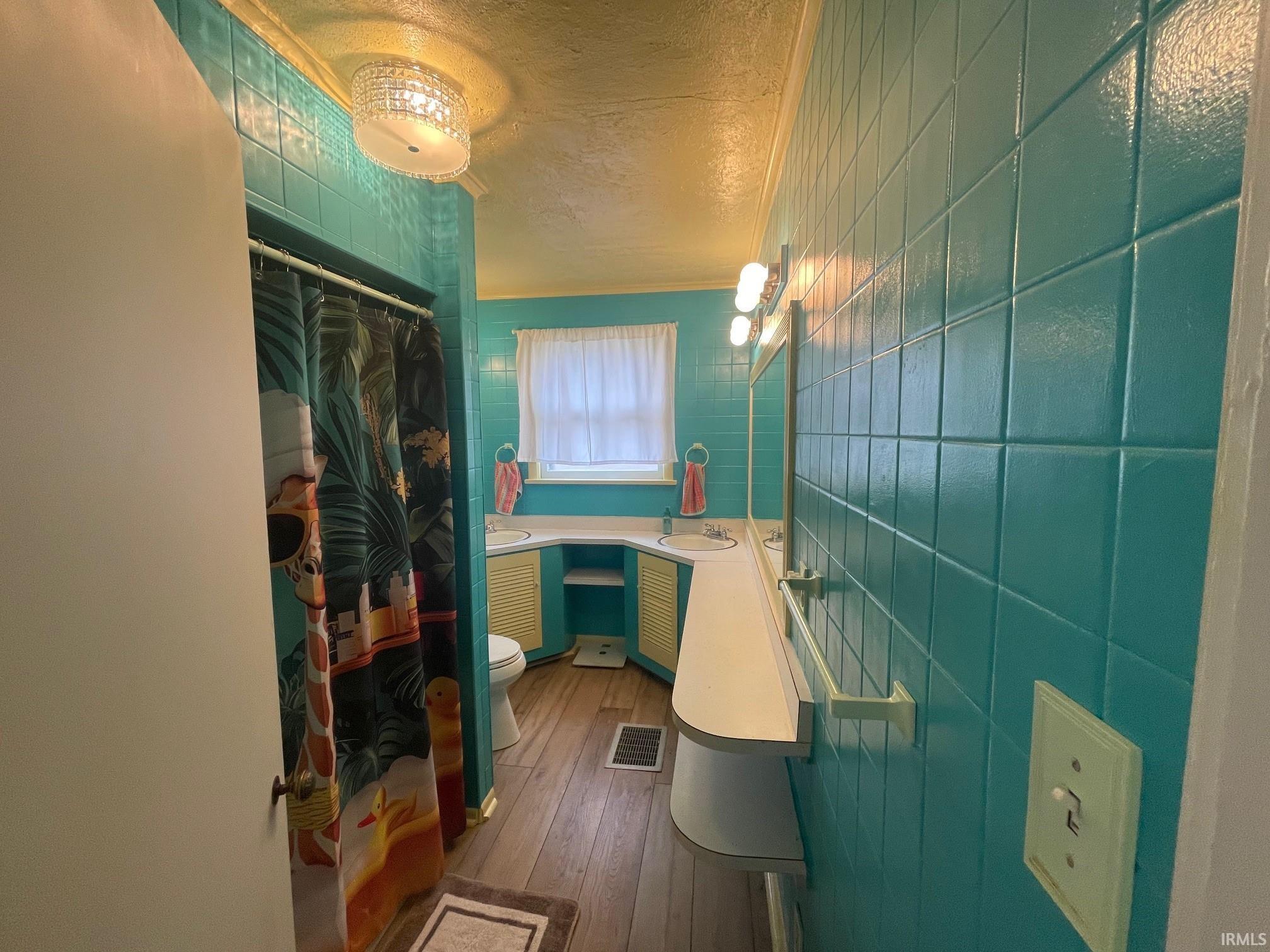 Full bathroom featuring a textured ceiling, vanity, curtained shower, tile walls.