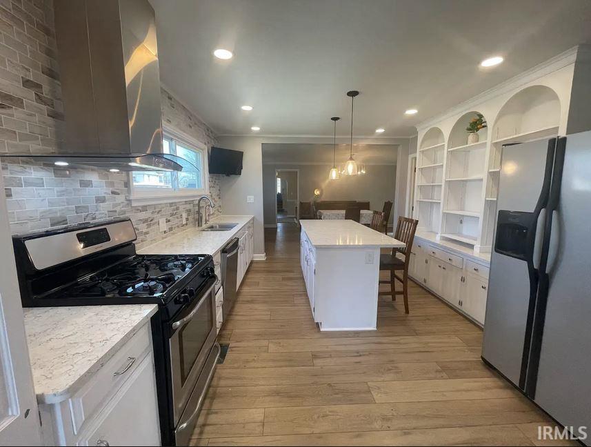 Kitchen with stainless steel appliances, hanging light fixtures, light stone counters, backsplash, and light wood-style flooring
