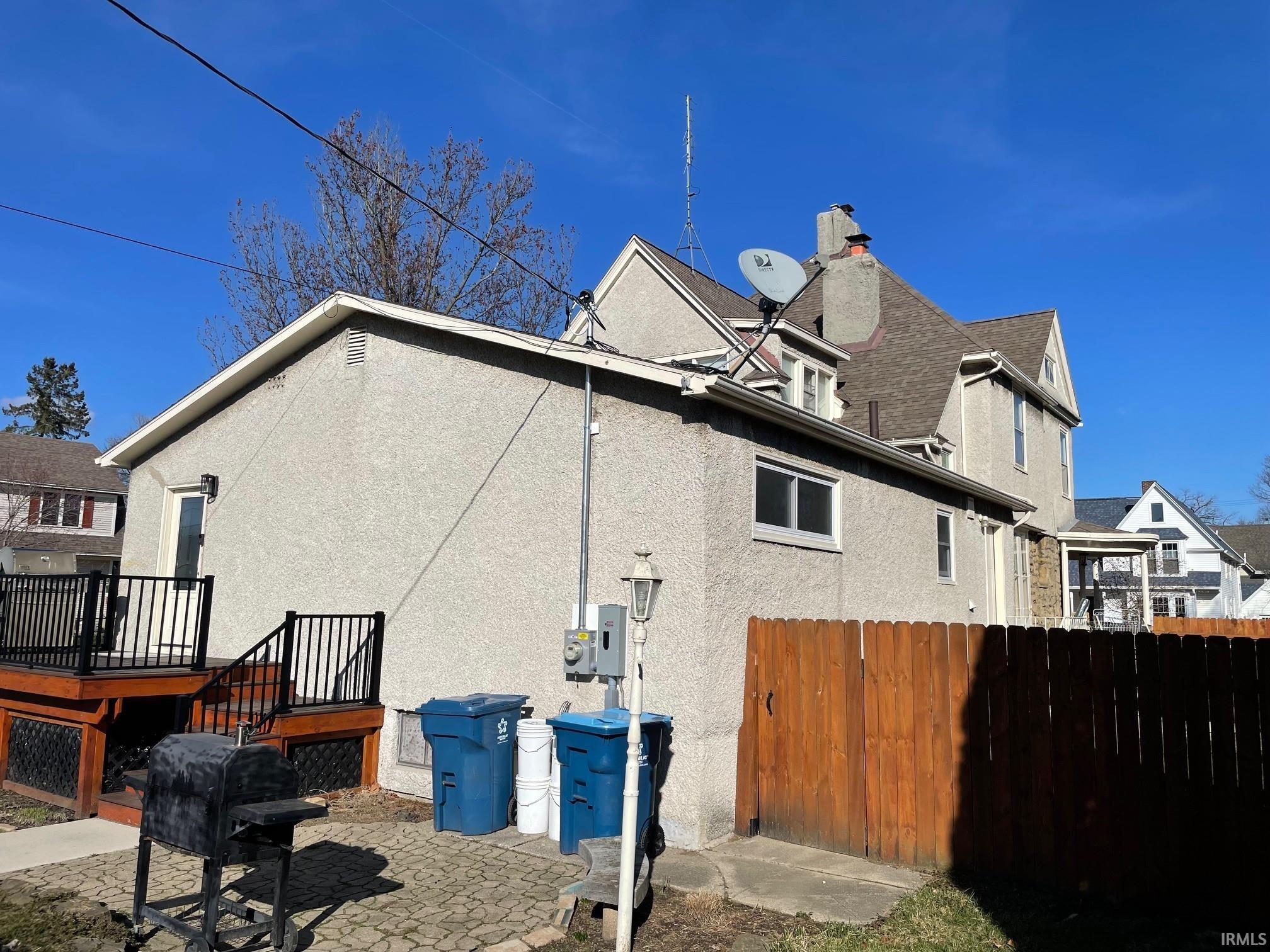 View of side of property featuring a wooden deck, stucco siding, and a patio area