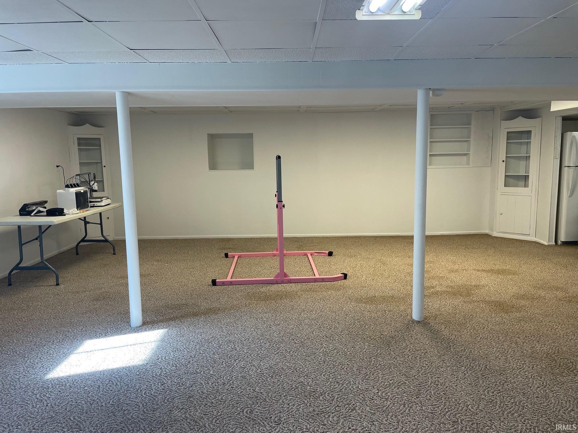 Finished below grade area featuring freestanding refrigerator, light colored carpet, a paneled ceiling, and built in features
