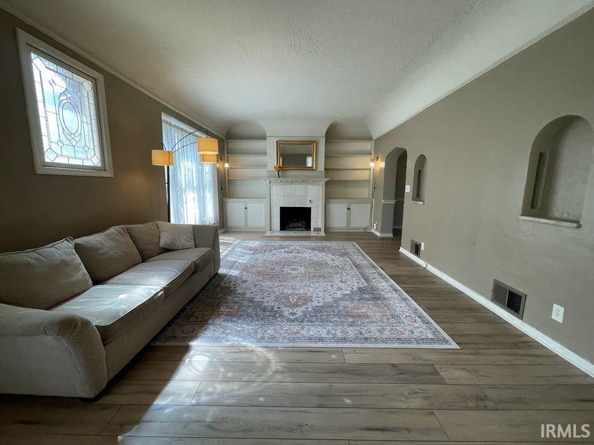 Living room featuring wood-type flooring, a fireplace with flush hearth, a textured ceiling, and arched walkways