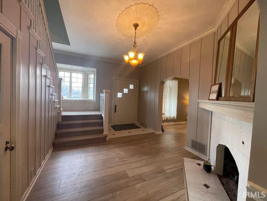 Foyer with arched walkways, light wood-style flooring, hanging lights, a gas fireplace, and crown molding.