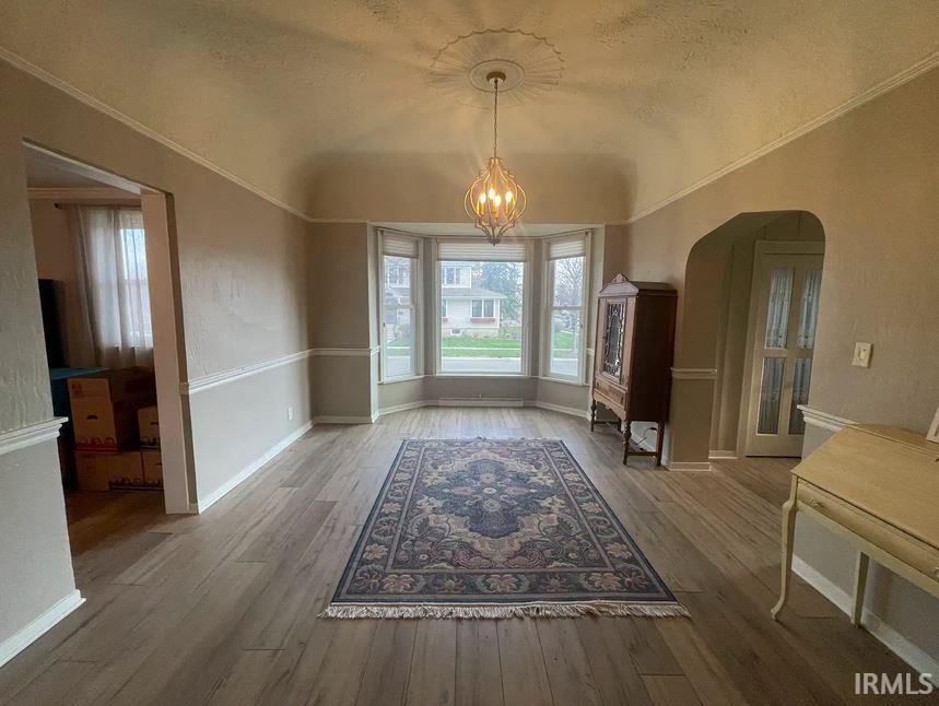 Parlor area with suspended lighting, arched walkways, light wood-style flooring, and ornamental molding.