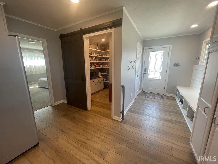 Pantry featuring a barn door, light wood-type flooring, crown molding, and recessed lighting and mud room with cubbies and hooks.
