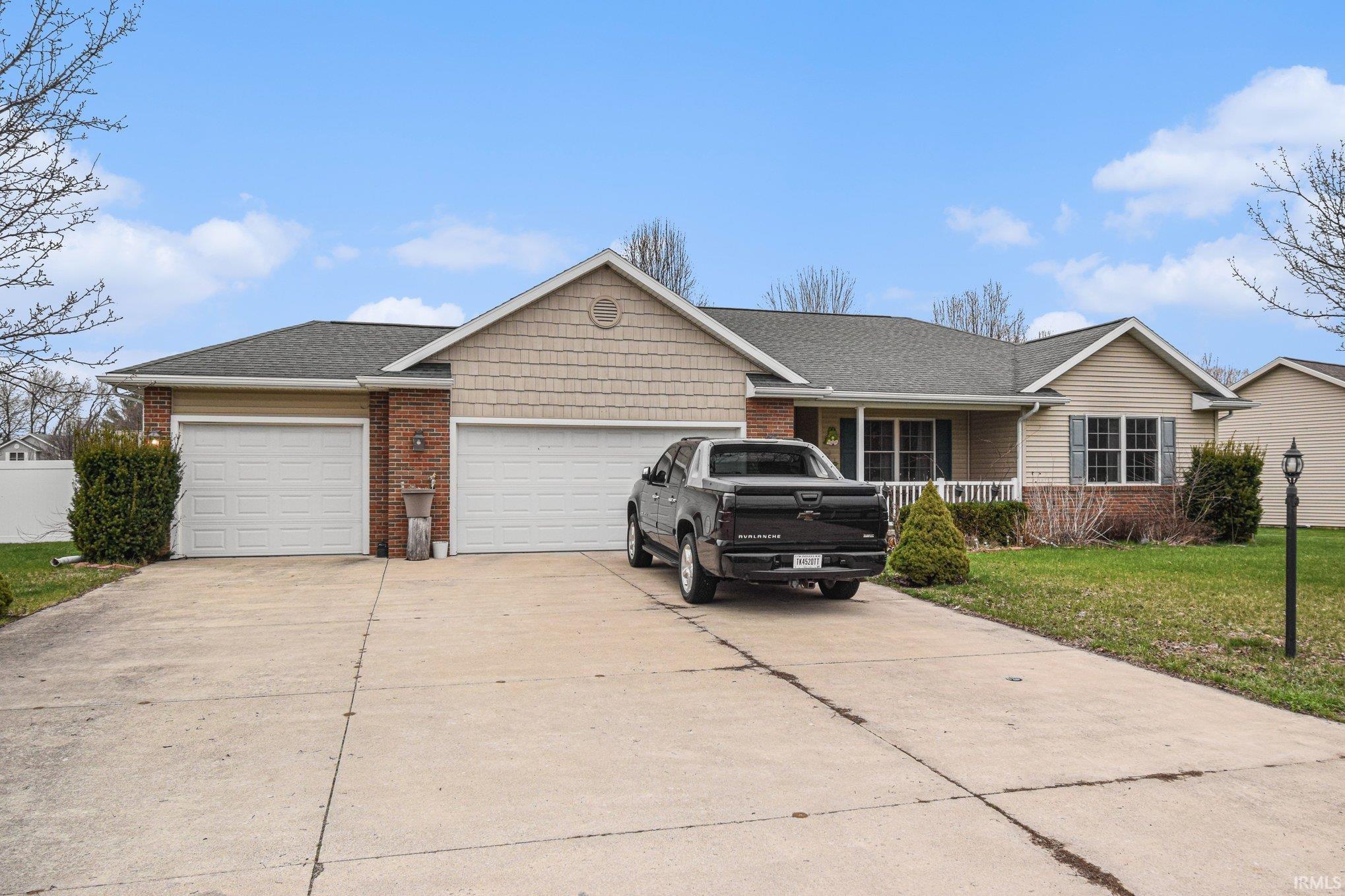 Ranch-style home with driveway, an attached garage, a front lawn, and brick siding