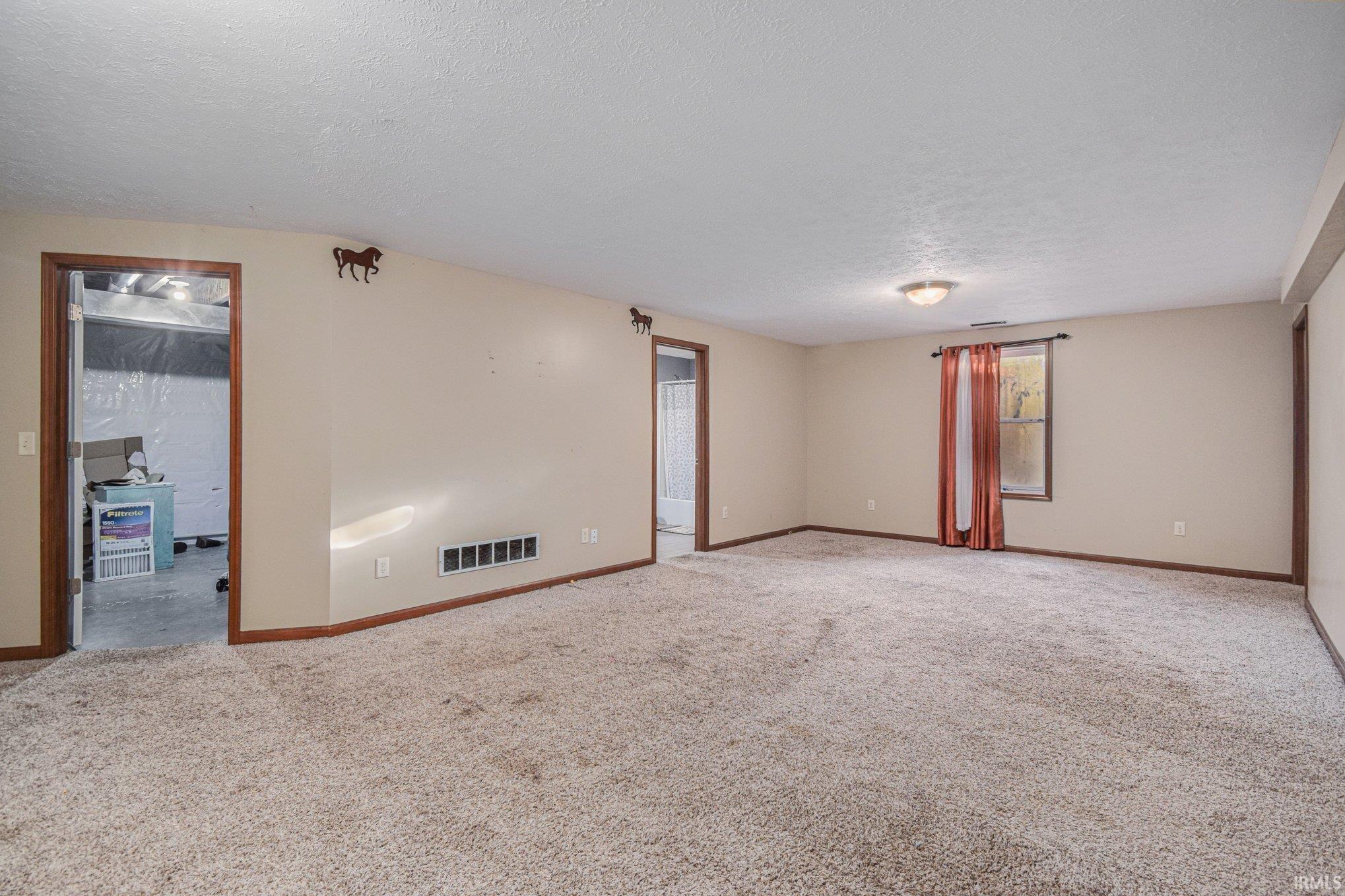 Carpeted spare room featuring a textured ceiling and baseboards