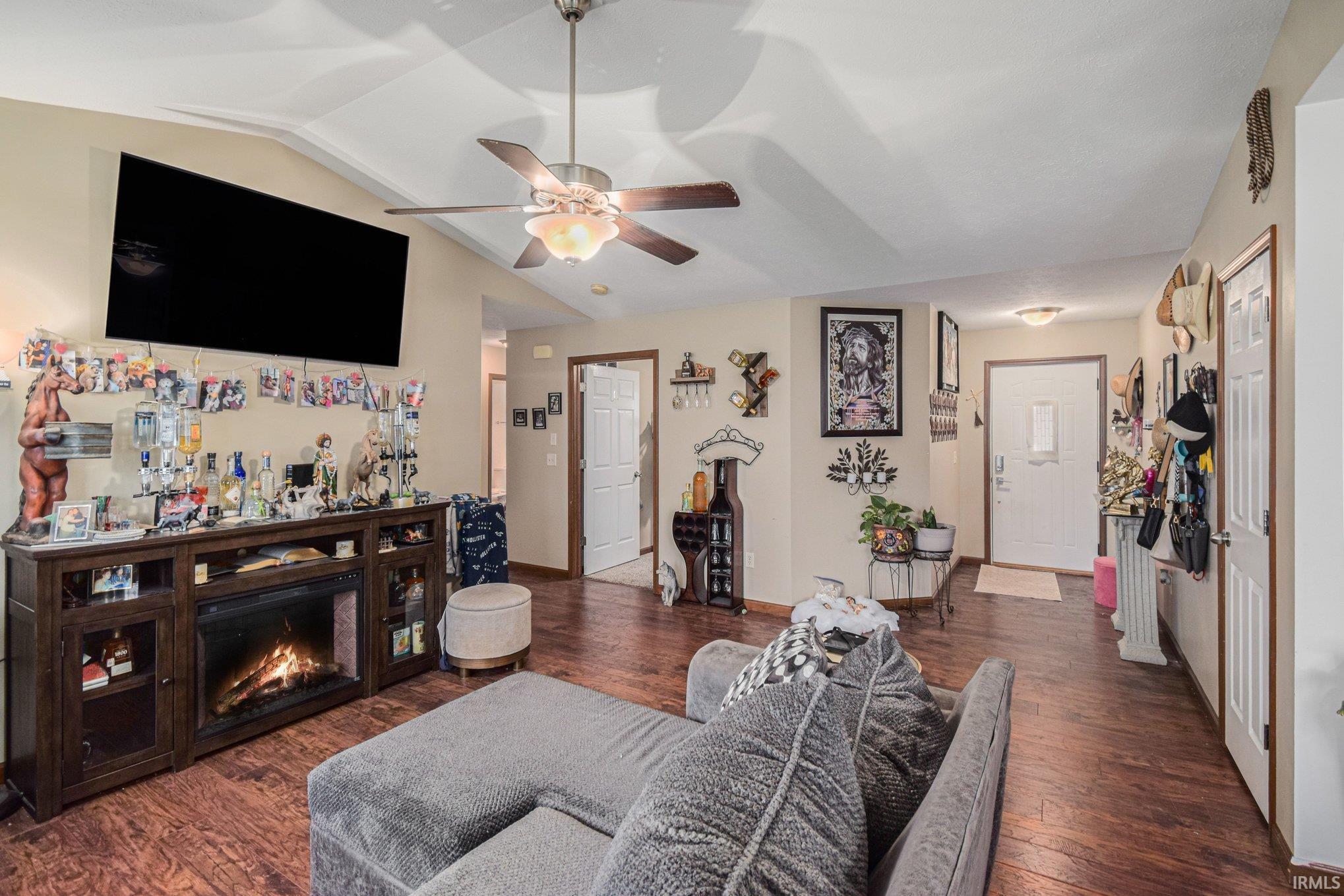 Living area with dark wood-type flooring, a warm lit fireplace, and ceiling fan